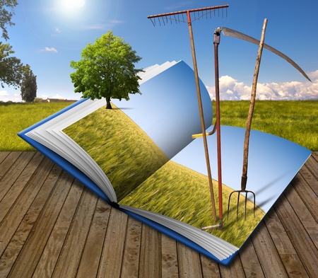 Open book with agricultural landscape and rake, scythe and pitchforkの写真素材