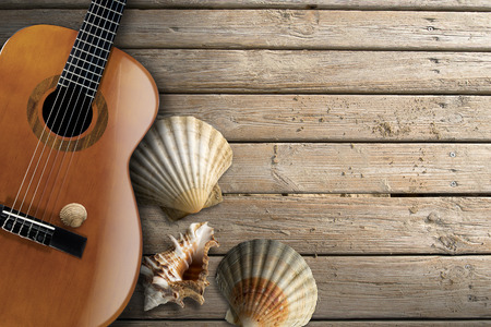 Acoustic brown guitar with four sea shells on beach wooden floor over summer sandの写真素材