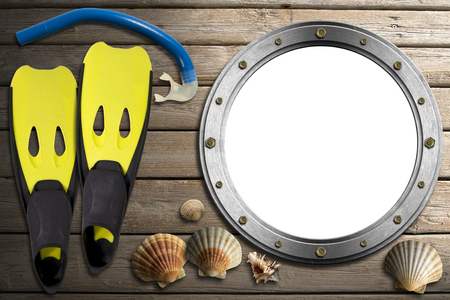 Metal empty porthole with seashells, yellow and black flippers and blue snorkel diving on wooden floor with sandの写真素材
