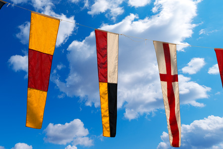 Three nautical flags hanging from a rope on a blue sky with clouds - representing the numbers 0, 9, 8の写真素材