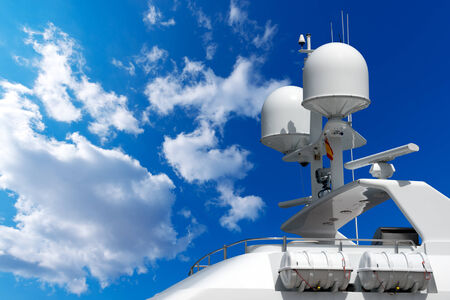 Detail of luxury white yacht with navigation equipment, radar, antennas and lifeboats on blue sky with cloudsの写真素材
