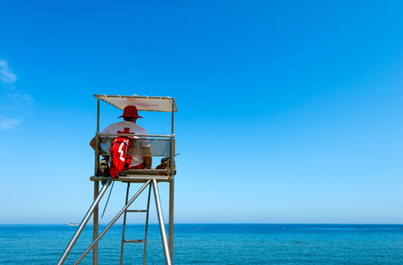Lifeguard sitting on surveillance steel tower watching the sea with portable radio transceiverのeditorial素材