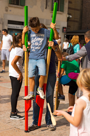 VERONA, ITALY - SEPTEMBER 21, 2014: Tocati, International festival of street games. An adult helps a unidentified child to walk on wooden stiltsのeditorial素材
