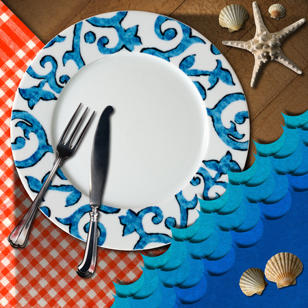Empty plate with fork and knife, red and white checkered tablecloth, seashells, blue waves and starfish. Table set for a seafood menuの写真素材