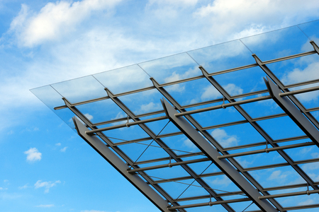 Detail of steel and glass roof of a modern building with blue sky and cloudsの写真素材