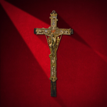 Ancient wooden cross with Jesus in silver on red velvet background with shadowsの写真素材