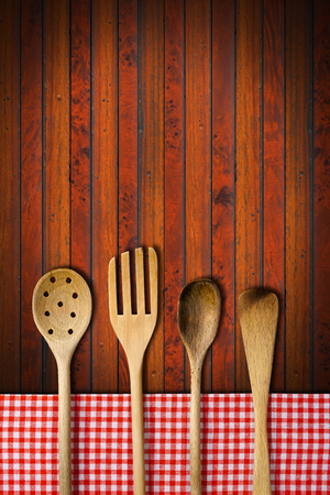 Four wooden kitchen utensils, fork, spoons and ladles on dark wooden background with red and white checkered tablecloth.の写真素材
