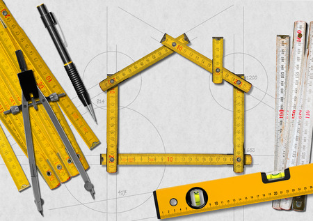 House project concept. Wooden meter ruler in the shape of house with a pencil, drawing compass, two meter tools and spirit level on a white paperの写真素材