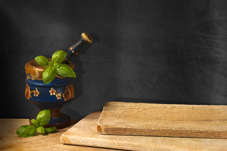 Empty blackboard on the wall, old wooden mortar and pestle with basil leaves. Concept of rustic cuisineの写真素材