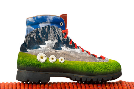 Climbing boot with a peak of mountain, green meadow and three daisy flowers inside. Isolated on white backgroundの写真素材