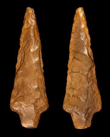 Macro photography of a prehistoric arrowhead in flint stone. Front and back, isolated on black backgroundの写真素材