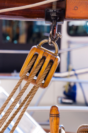 Detail of an old wooden pulley with ropes hanging on a boom of an old sailing boat