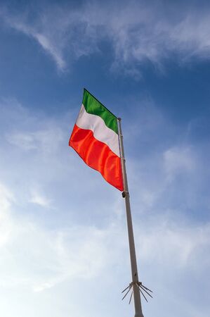National Italian flag with pole flowing in the wind on a blue sky with clouds
