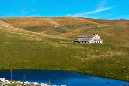 Typical farm house abandoned (Malga) and small lake in Lessinia for the breeding of cows, Prealps of Veneto, Verona, Italyのeditorial素材