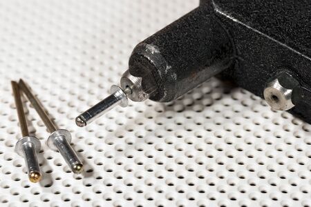 Detail of an old rivet gun (hand riveter) with rivets on a white background with holesの写真素材