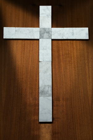 White marble cross on a wooden brown background with dark shadowsの写真素材