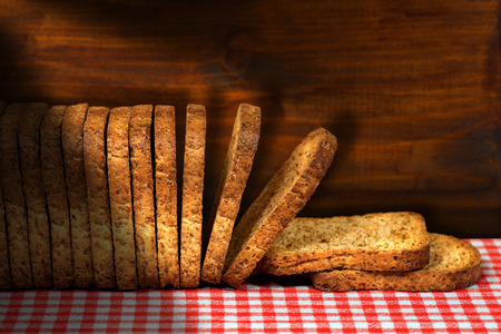 Row of healthy rusks of wholemeal flour on a table with red and white checkered tablecloth and wooden dark wallの写真素材