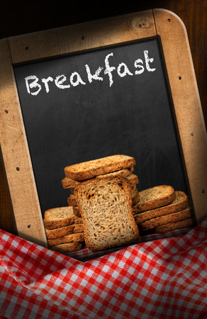 Rusks of wholemeal flour in a blackboard with text Breakfast. On a table with red and white checkered tableclothの写真素材