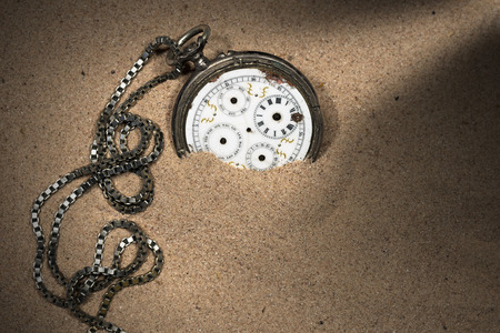 Old and broken pocket watch with chain and without watch hands partially buried in the sandの写真素材