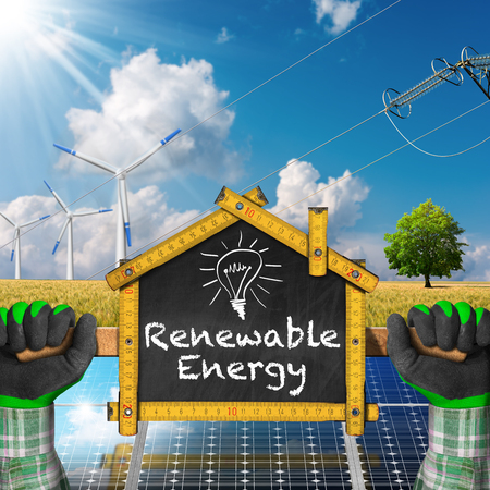 Hands with work gloves holding a wooden ruler in the shape of house with renewable energies. Concept of ecological house projectの写真素材