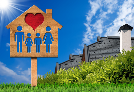 Sign in the shape of a wooden model house with a family and red heart. On green grass with two roofs of housesの写真素材