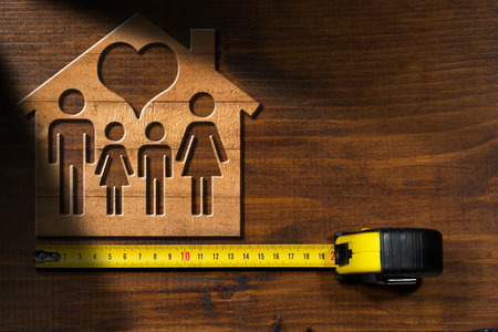 Wooden model house with a symbol of family and heart. On a wooden desk with a tape rulerの写真素材