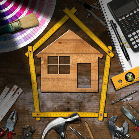 Home improvement concept - Wooden model house with work tools and a calculator on a wooden desk