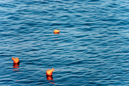 Three orange buoys for mooring boats on the surface of the water. Mediterranean sea, Italy