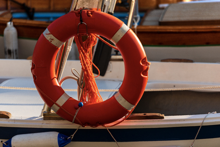 Close-up of an orange and white lifebuoy with ropes hanging on the side of a small boatの写真素材