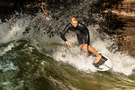 MUNICH, GERMANY - SEPT 8, 2018: A man surfing in the waves of the Eisbach River in downtown of...