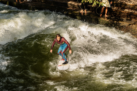 MUNICH, GERMANY - SEPT 8, 2018: A man surfing in the waves of the Eisbach River in downtown of Munich. It forms a standing wave right at the entrance of the Englischer Garten (English Garden) and is a popular surfers meeting point of the city.のeditorial素材