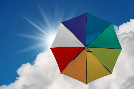 Multicolor umbrella flying in a blue sky with clouds and sun raysの写真素材