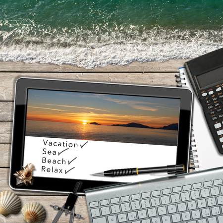 Dreaming summer vacation at work. Workspace with tablet computer, keyboard, calculator, sea waves, landscape with sunset and texts, Vacation, Sea, Beach and Relaxの写真素材
