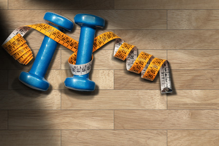 Two small blue dumbbells for women, for workout or fitness (free weights) and a orange tape measure on a wooden gym floor (parquet) with copy spaceの写真素材