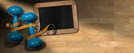Two old blue dumbbells for workout or fitness (free weights) with orange tape measure and empty blackboard on a wooden gym floor, parquet.の写真素材
