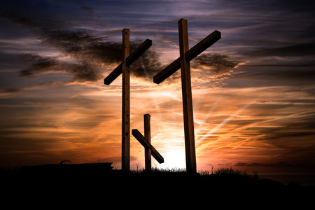 Silhouette of three wooden crosses above the hill with dramatic sky and sun rays at sunset. Religious symbol of good fridayの写真素材