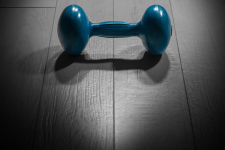 Close-up of an old blue dumbbell for weight training or fitness on a gray gym floorの写真素材