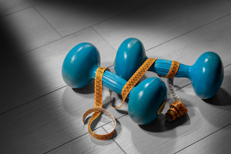 Close-up of two old blue dumbbells for weight training or fitness and a tape measure on a gray gym floorの写真素材