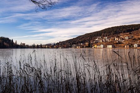 Serraia Lake (Lago della Serraia) frozen in winter and the small town of Baselga di Pine. Trento province, Trentino Alto Adige, Italy, Europeの写真素材