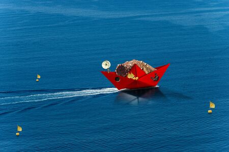Red paper fishing boat with fishing nets, buoys with flags, winch and anchor, sails in the blue sea....