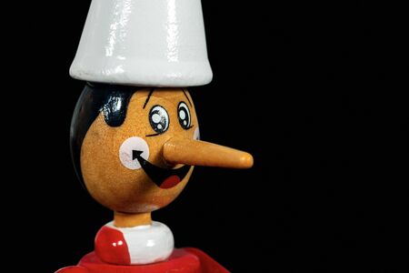 Close-up of a Pinocchio wooden toy isolated on black background with copy space. Character from the fairy tale written by Carlo Collodiの写真素材