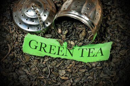 Close-up of many dried leaves of green gunpowder tea with steel strainer and a piece of paper with text Green Teaの写真素材