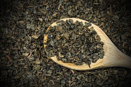 Extreme close up of dried leaves of green gunpowder tea on a wooden spoon, with many rolled up leaves on the backgroundの写真素材