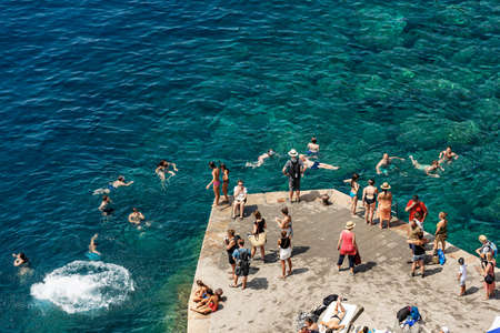 VERNAZZA, LIGURIA, ITALY - JULY 22, 2019: a group of people swim and sunbathe in the sea of the small village of Vernazza, Cinque Terre, UNESCO world heritage site. La Spezia, Liguria, Italy, Europeのeditorial素材