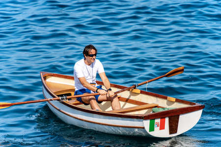 GULF OF LA SPEZIA, LIGURIA, ITALY - JULY 21th, 2019: A man on a small wooden rowboat in the blue Mediterranean sea in front of the ancient Tellaro village, Liguria, Italy, Europeのeditorial素材