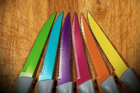 Close-up of set of six colored table knives on a wooden cutting board