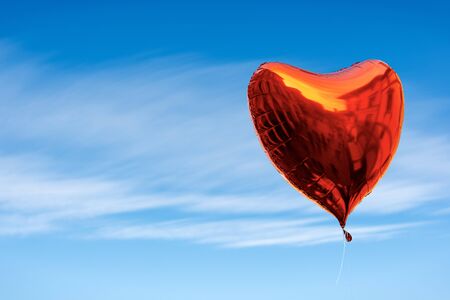 Close-up of a red balloon in the shape of a heart, with the reflections of a city, in a blue sky...