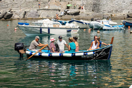 VERNAZZA, LIGURIA, ITALY - JULY 22, 2019: port of the ancient and famous village of Vernazza, a local man rows on a small wooden boat with six tourists on board. Cinque Terre, National park in Liguria, La Spezia, Italy, Europe. UNESCO world heritage siteのeditorial素材