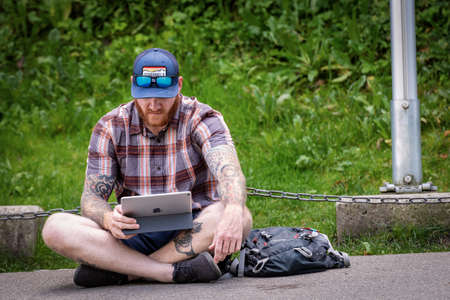 SCHWANGAU, GERMANY - SEP 9, 2018: a young man sitting cross-legged on the roadside using his Apple...