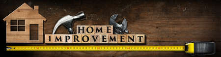 Text Home Improvement, made of wooden blocks on a wooden table with work tools (hammer, adjustable wrench and yellow tape measure) and stylized model house.の写真素材